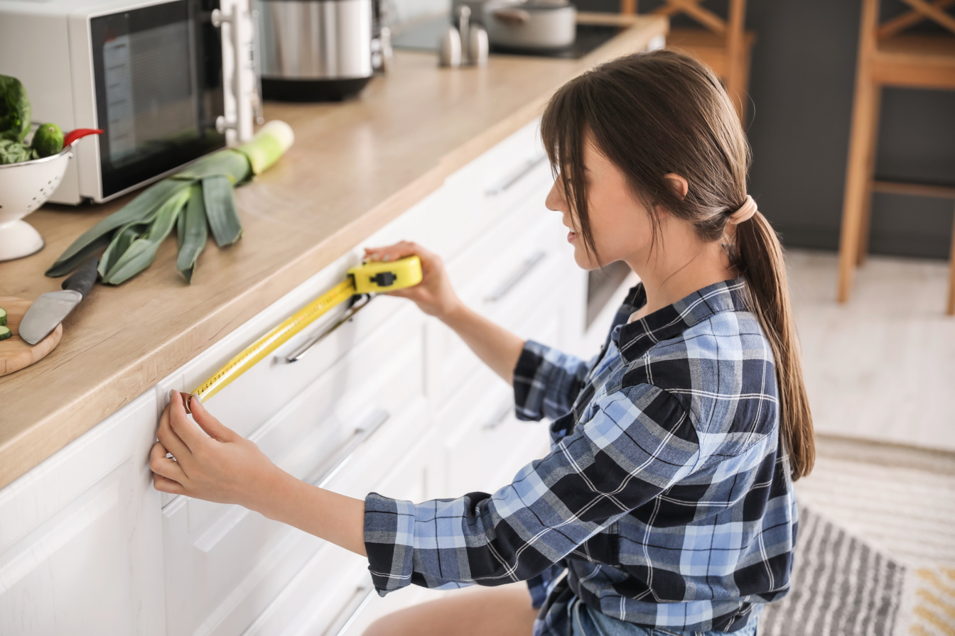 Young Woman Measuring Furniture in Kitchen